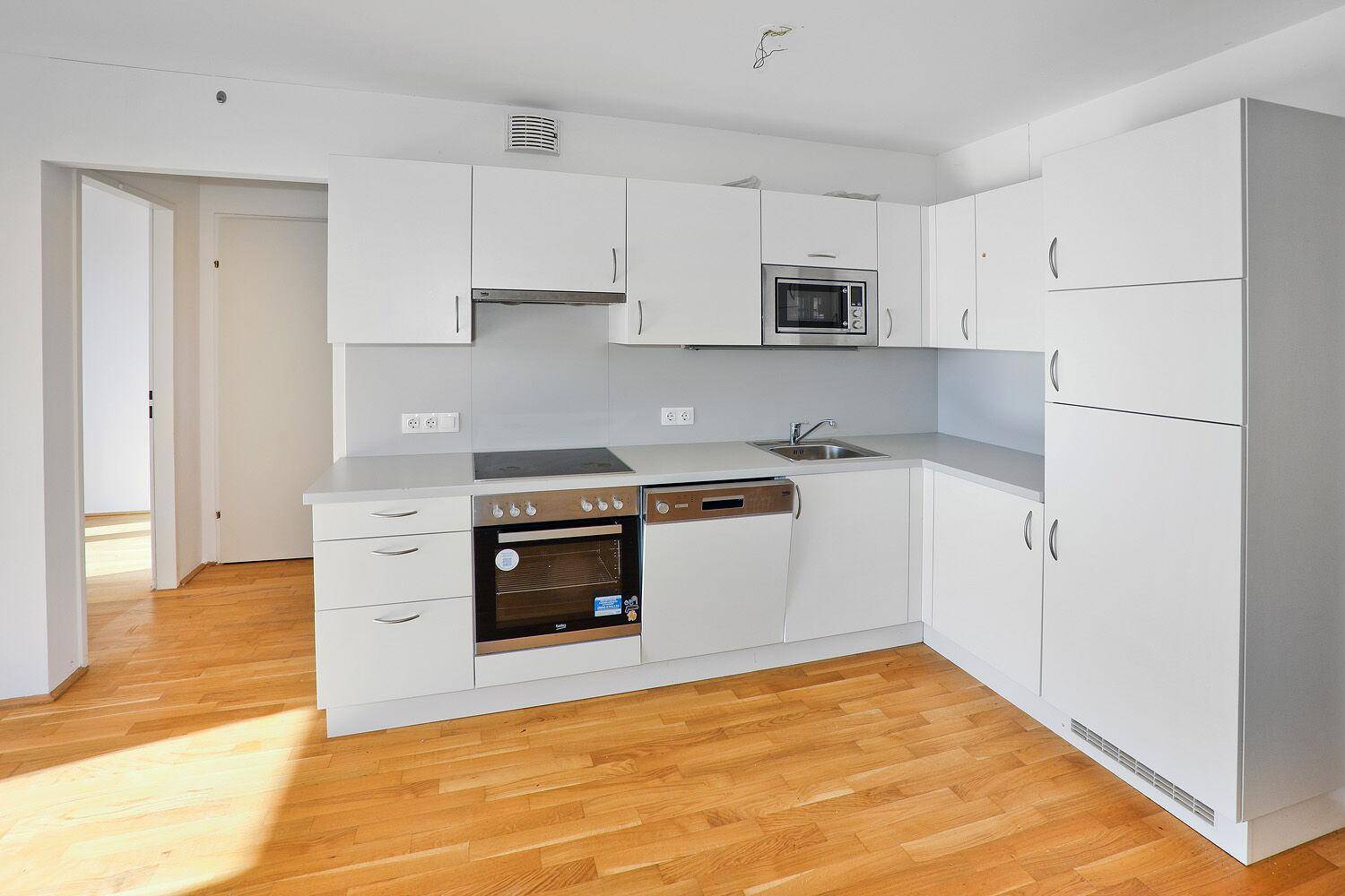Moderne Einbauküche in Weiß mit integrierten Geräten und hellem Parkettboden.