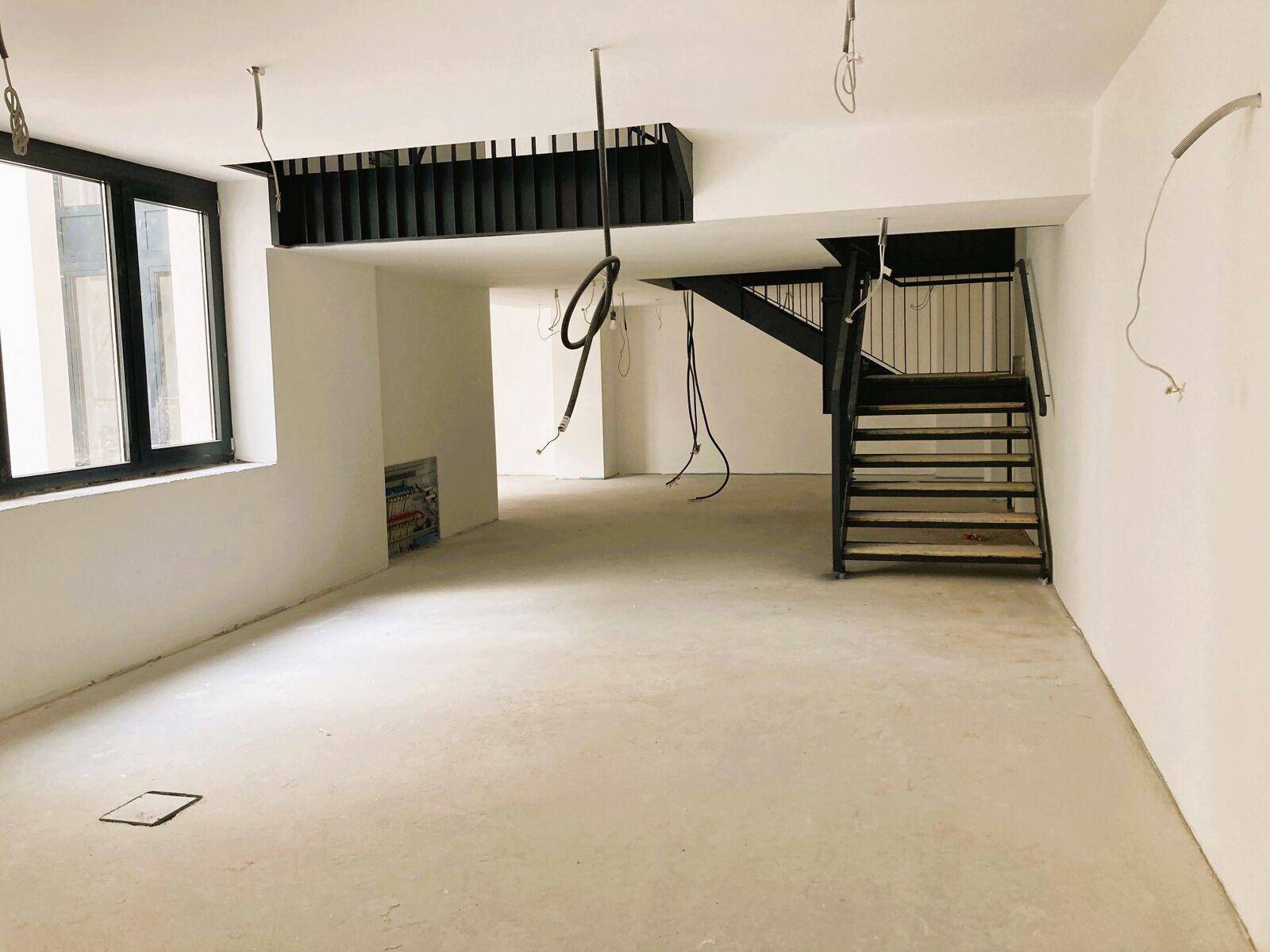 Großer, heller Innenraum im Rohbau mit Treppe zu einer Galerie und großen Fenstern, bereit für den Ausbau.