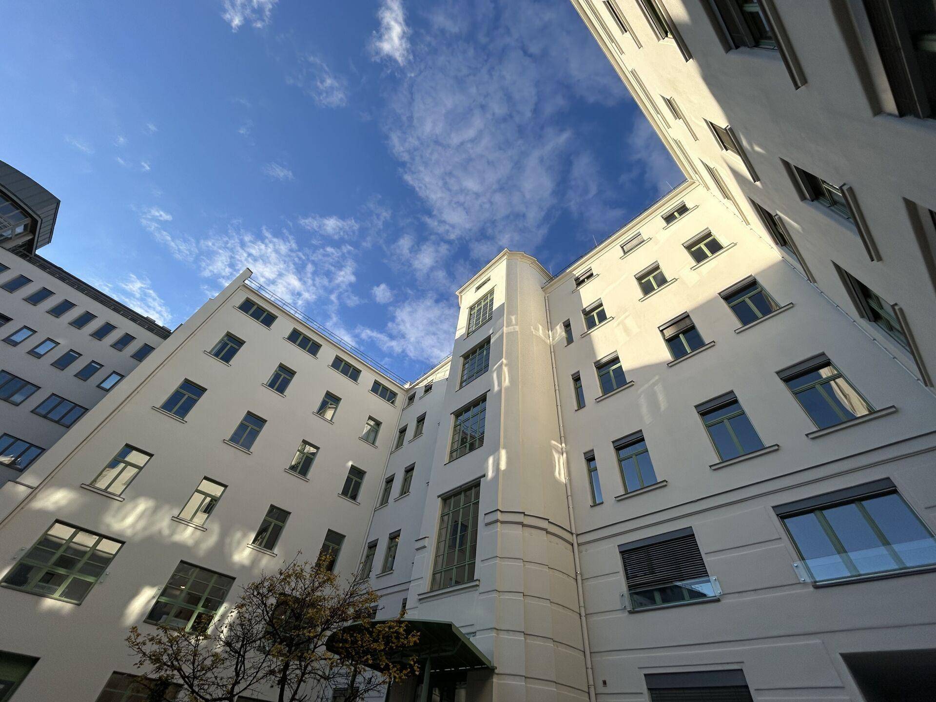 Blick in den hellen Innenhof eines modernen Gebäudes mit vielen Fenstern und klarem blauen Himmel.