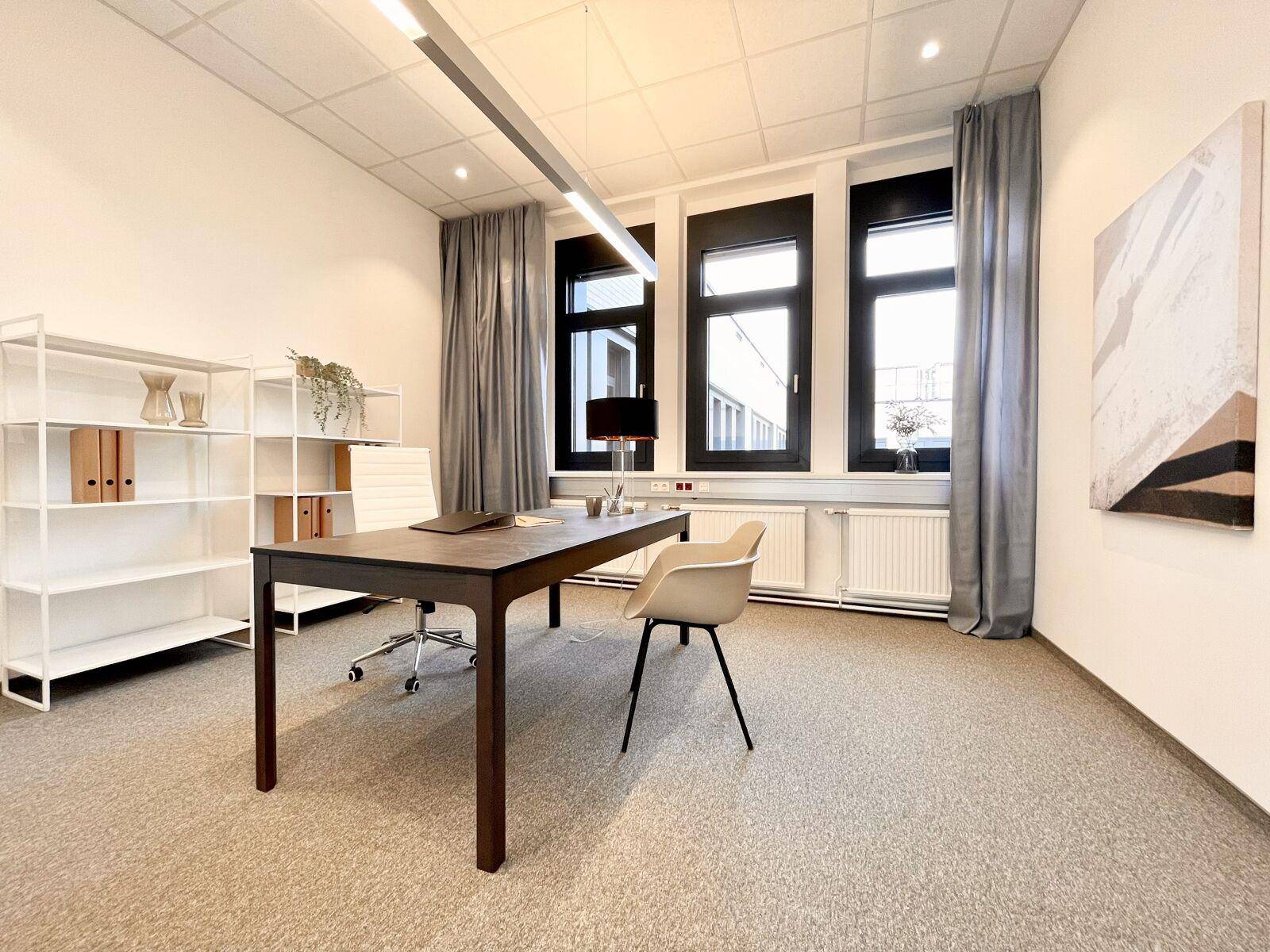 Modernes Einzelbüro mit Schreibtisch, Bürostuhl, weißen Regalen und großen Fenstern mit grauen Vorhängen.