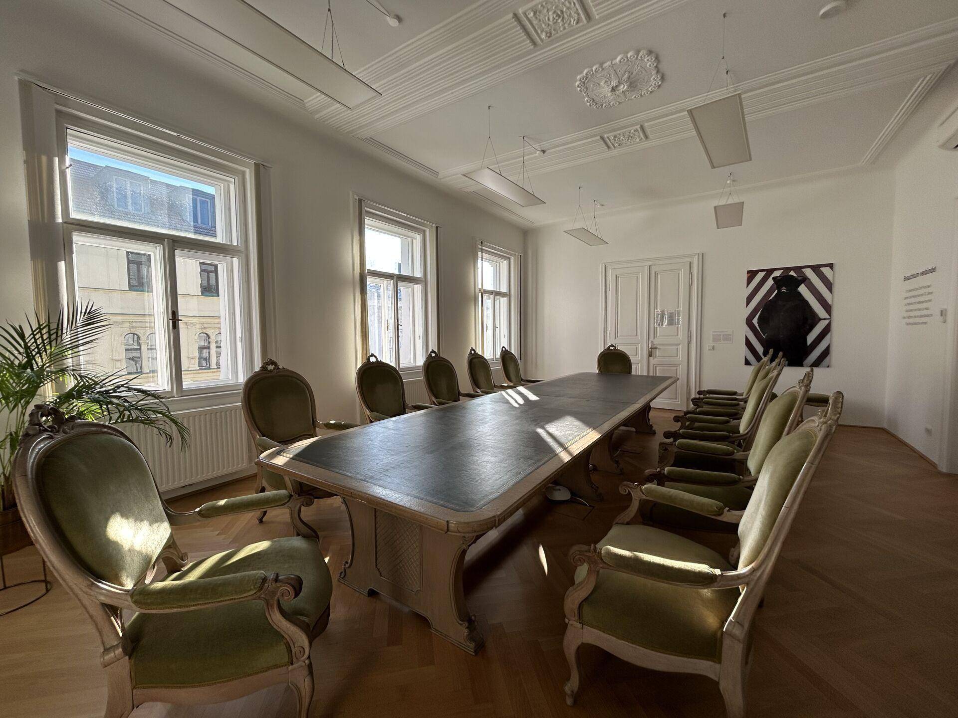 Geräumiger Konferenzraum mit großem Tisch, vielen Stühlen und Fischgrätparkett, ergänzt durch eine Stuckdecke.