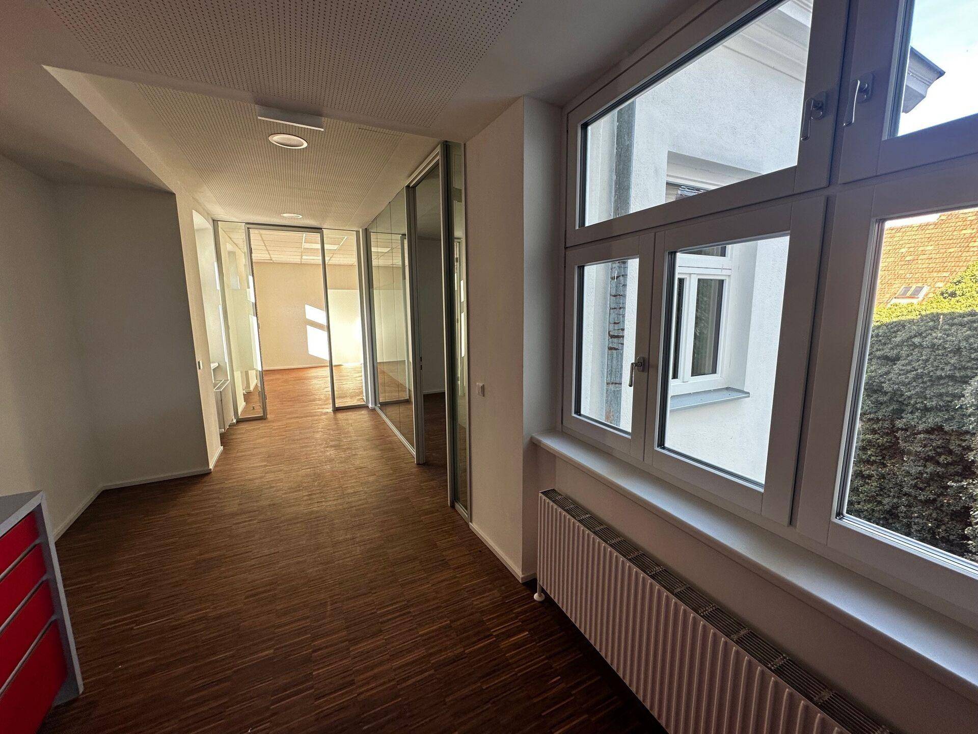 Heller Flur mit Holzboden und Fenstern, die Tageslicht in den Bürobereich lassen.