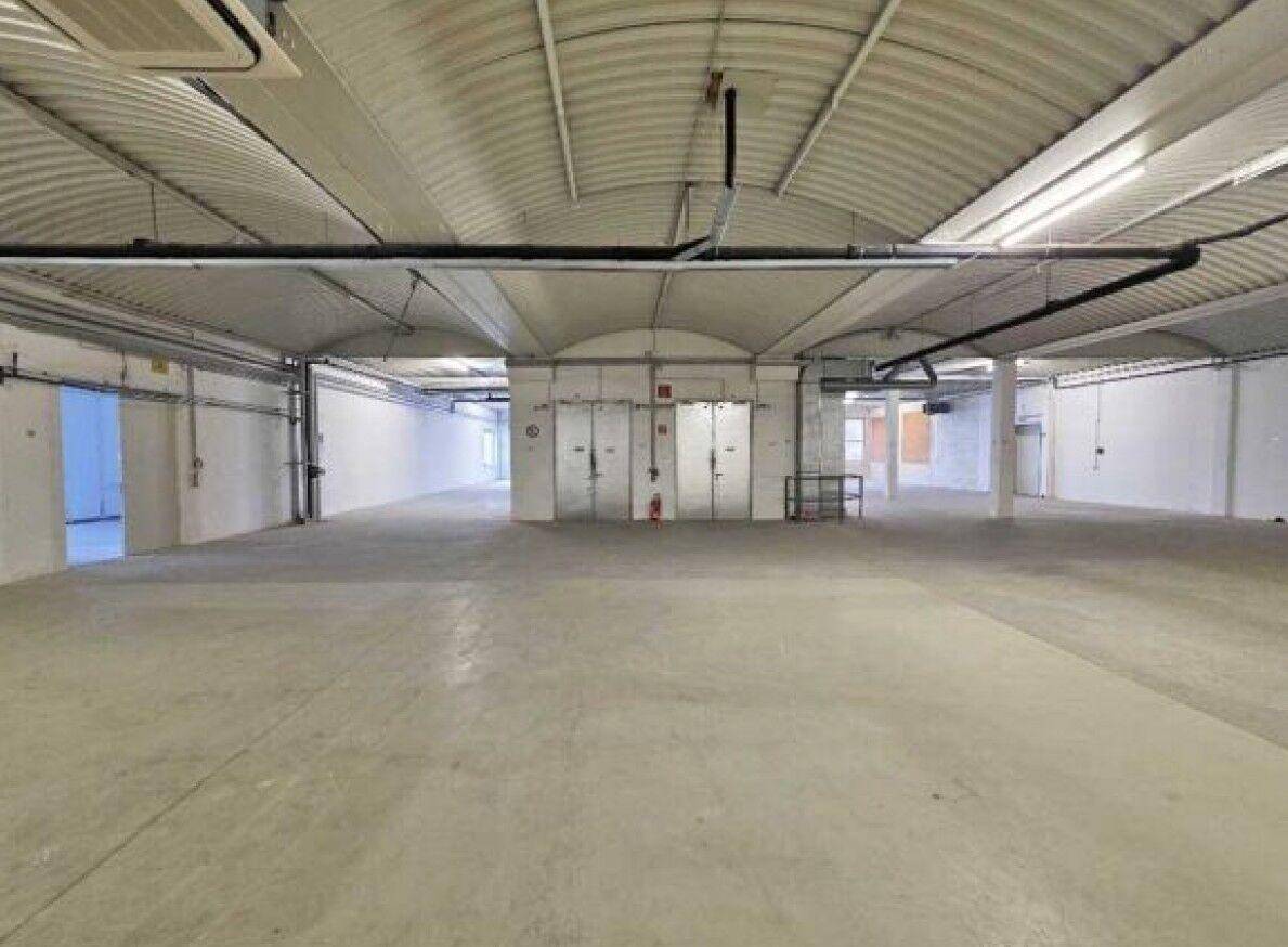 Weitläufige Lagerfläche mit gewölbter Decke, Betonboden und mehreren Zugangstüren im Hintergrund.