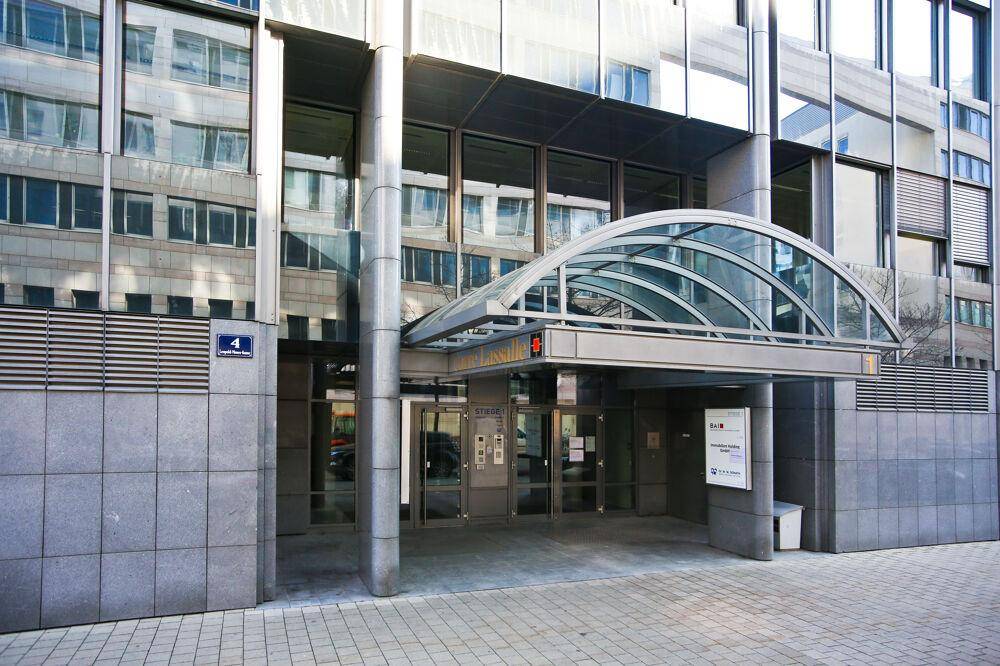 Eingangsbereich eines modernen Bürogebäudes mit Glasüberdachung und Granitverkleidung an der Fassade.