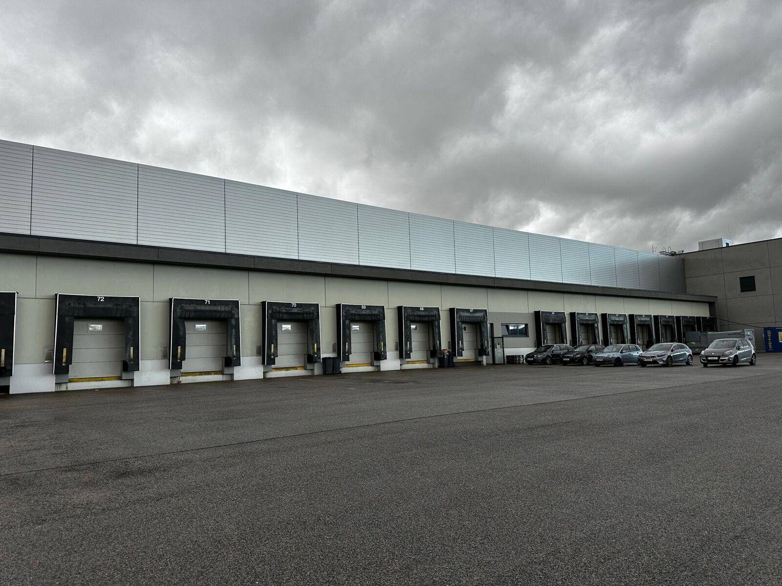 Reihe von Laderampen an der Fassade eines modernen Logistikgebäudes unter einem bewölkten Himmel.