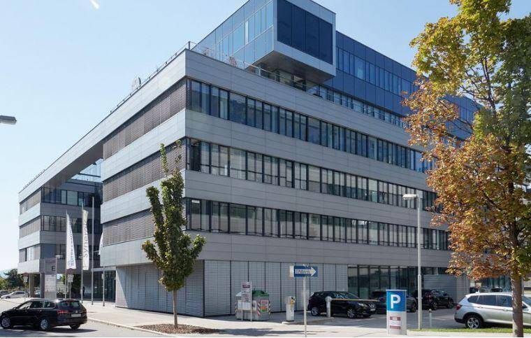 Ansicht eines modernen Bürokomplexes mit Parkplätzen, Bäumen und einer klaren architektonischen Gestaltung.