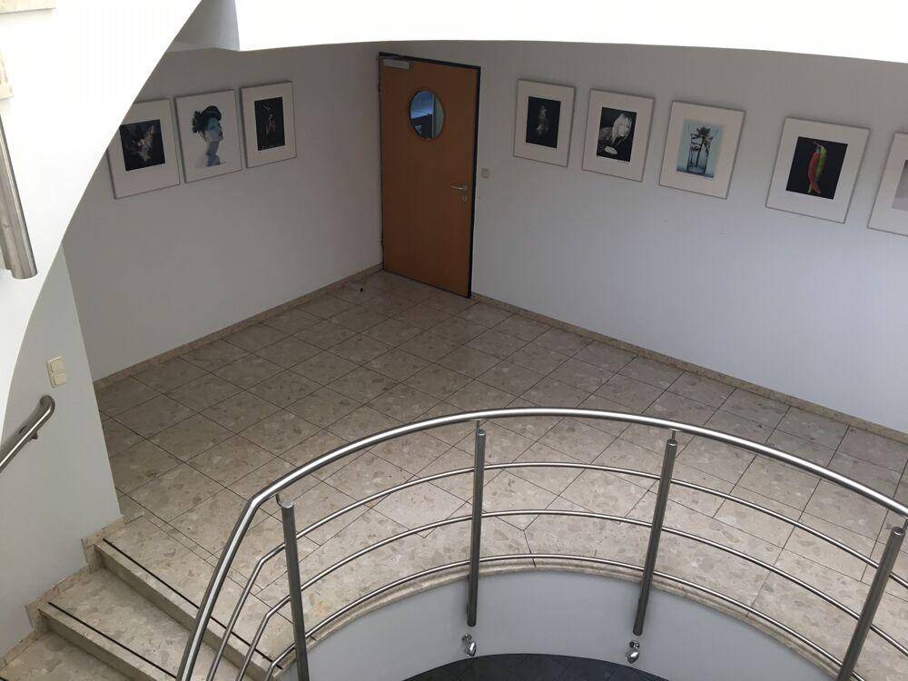 Elegantes Treppenhaus mit geschwungener Edelstahltreppe und hellen Fliesenböden, dekoriert mit Kunstwerken.