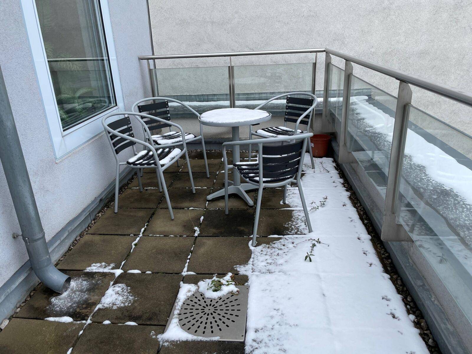 Kleiner Balkon mit Outdoor-Möbeln und Fliesenboden, teilweise mit Schnee bedeckt, bietet einen Blick auf die Umgebung.