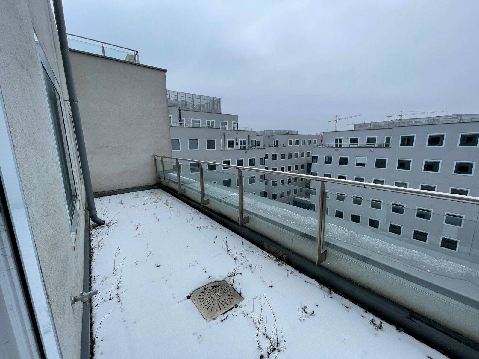 Große Dachterrasse mit Glasgeländer und Fliesenboden, teilweise mit Schnee bedeckt, bietet weite Aussicht.