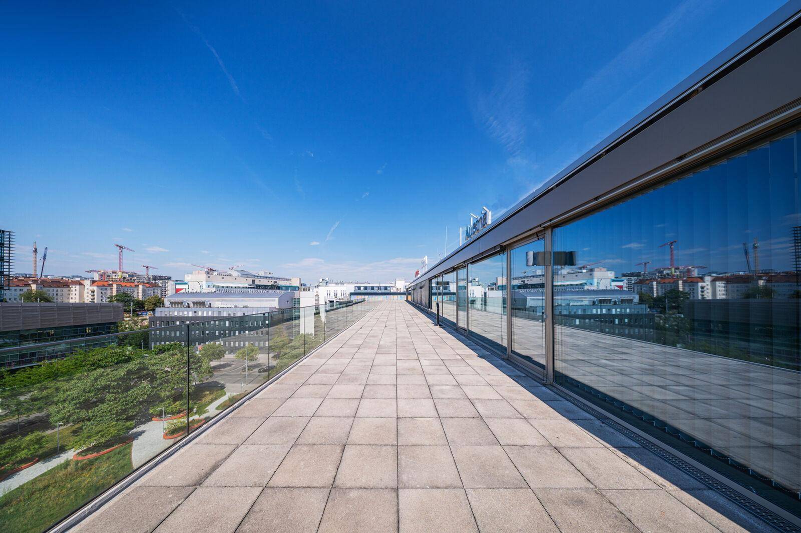 Weitläufige Dachterrasse mit Fliesenboden und Glasgeländer bietet einen weiten Blick über die Stadt.