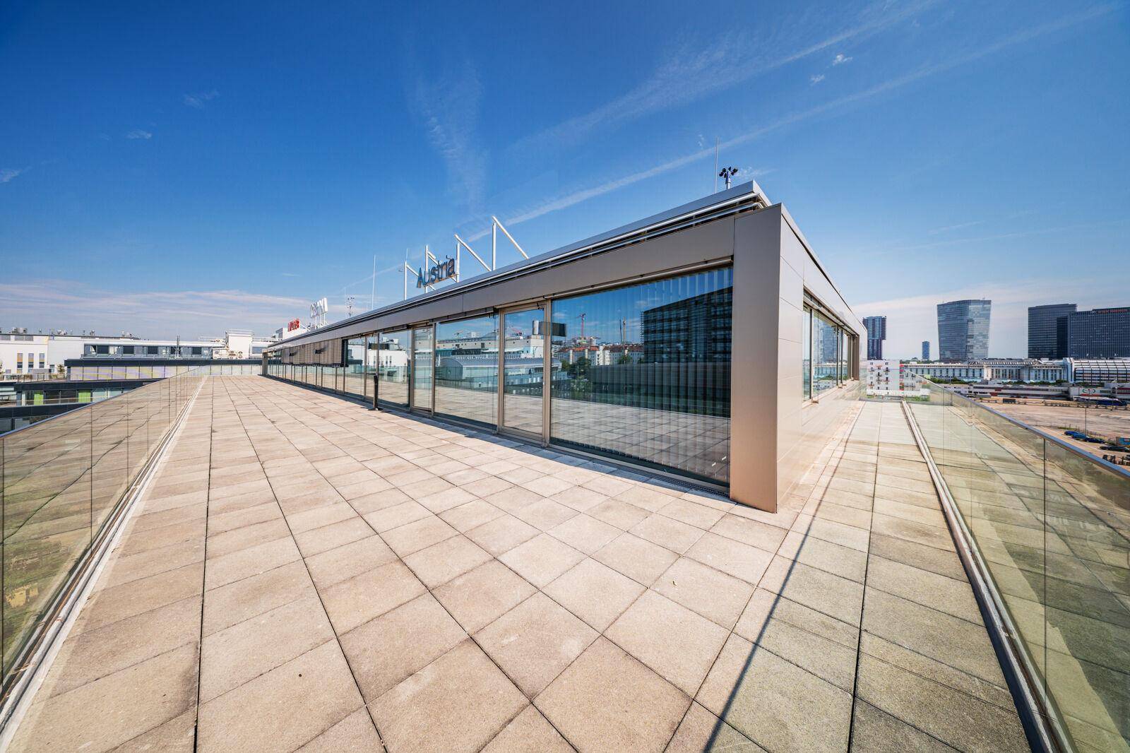 Große Dachterrasse mit Fliesen und Glasbrüstung, die einen Panoramablick auf die Umgebung ermöglicht.