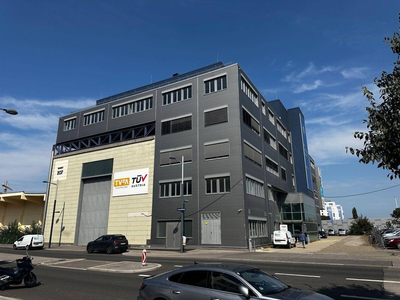 Modernes Bürogebäude mit grauer Fassade und großen Fenstern an einer belebten Straße in der Stadt.