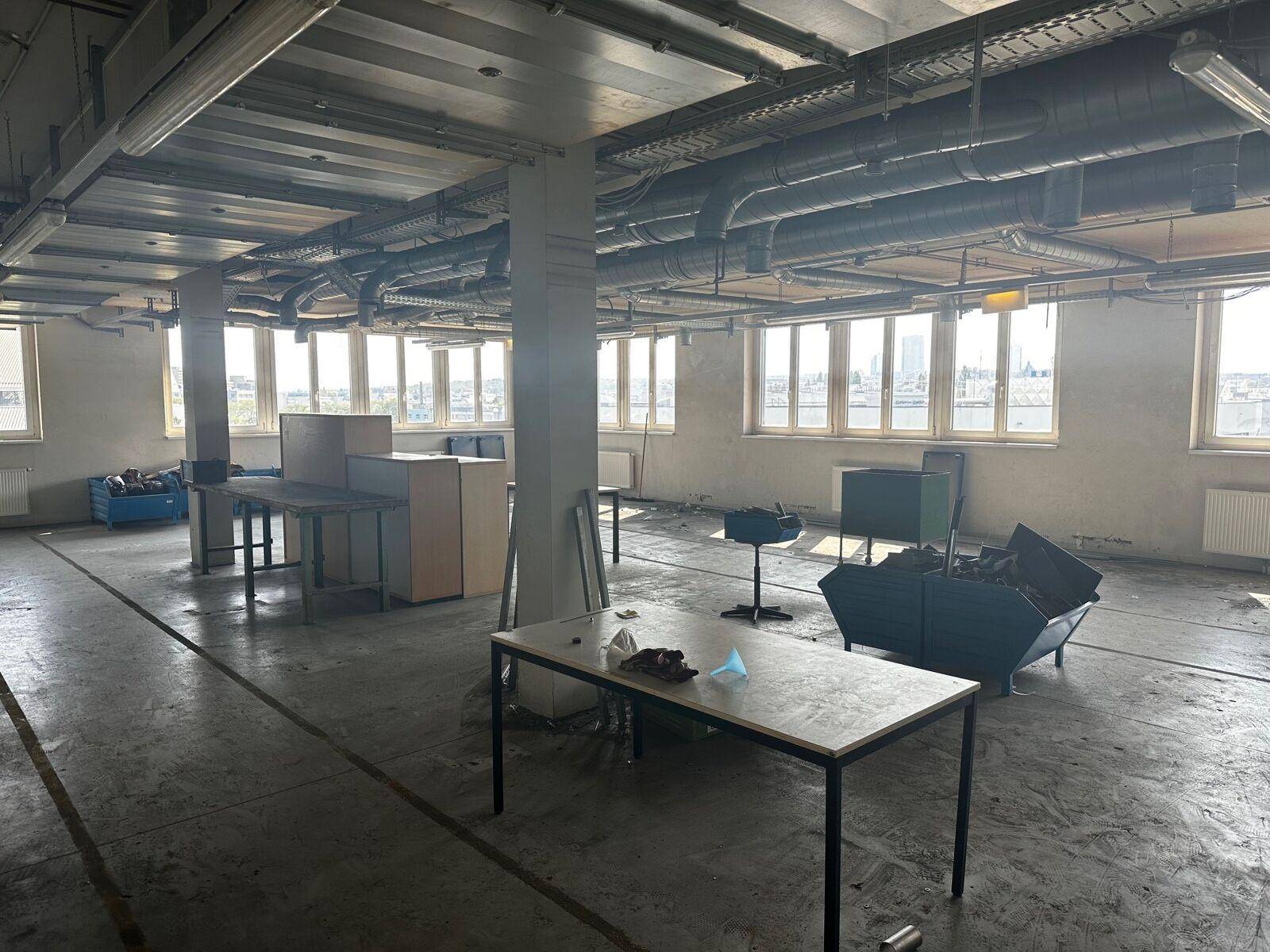Großraumbüro in Renovierung mit Betonboden, vielen Fenstern und sichtbaren Lüftungsrohren an der Decke.