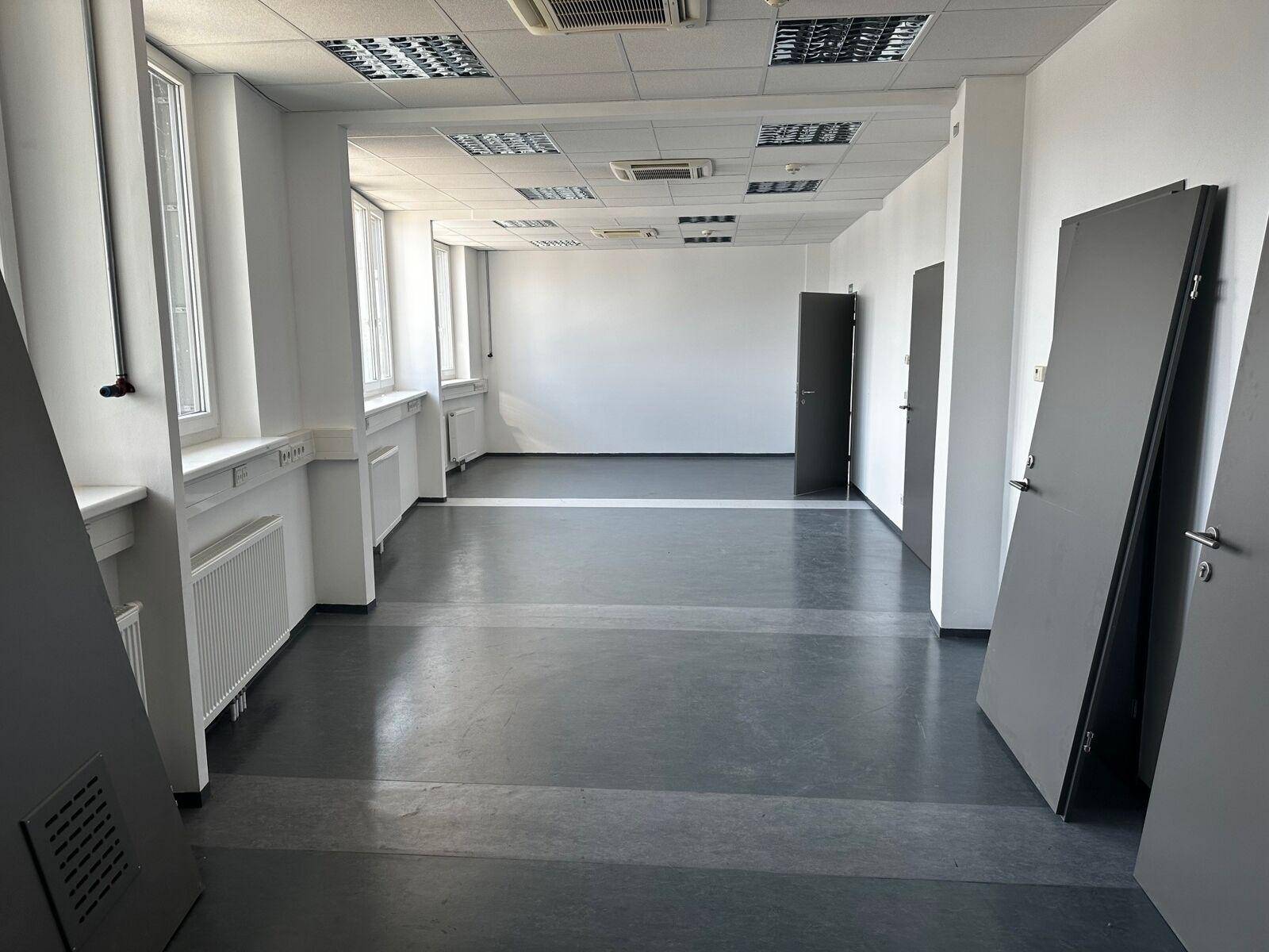 Heller Büroraum mit großen Fenstern, Teppichfliesen und abgehängter Decke, in gutem Zustand.