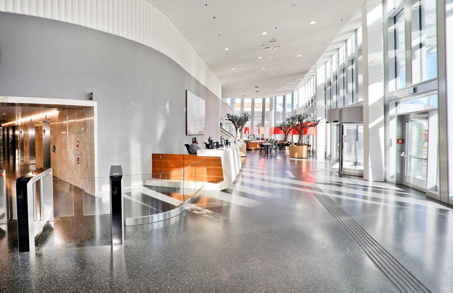 Geräumige, moderne Lobby mit Empfangsbereich, hohen Decken und viel Tageslicht durch die Glasfassade.