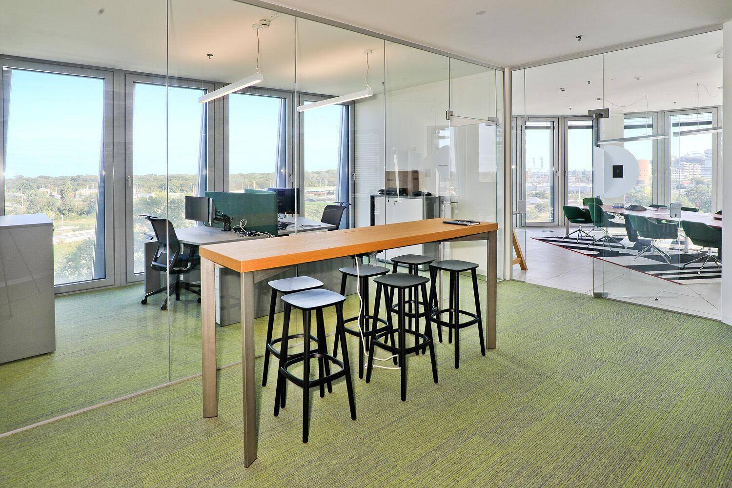 Modernes Büro mit Glaswänden, Arbeitsplätzen und einem Stehtisch, ideal für Teamarbeit.