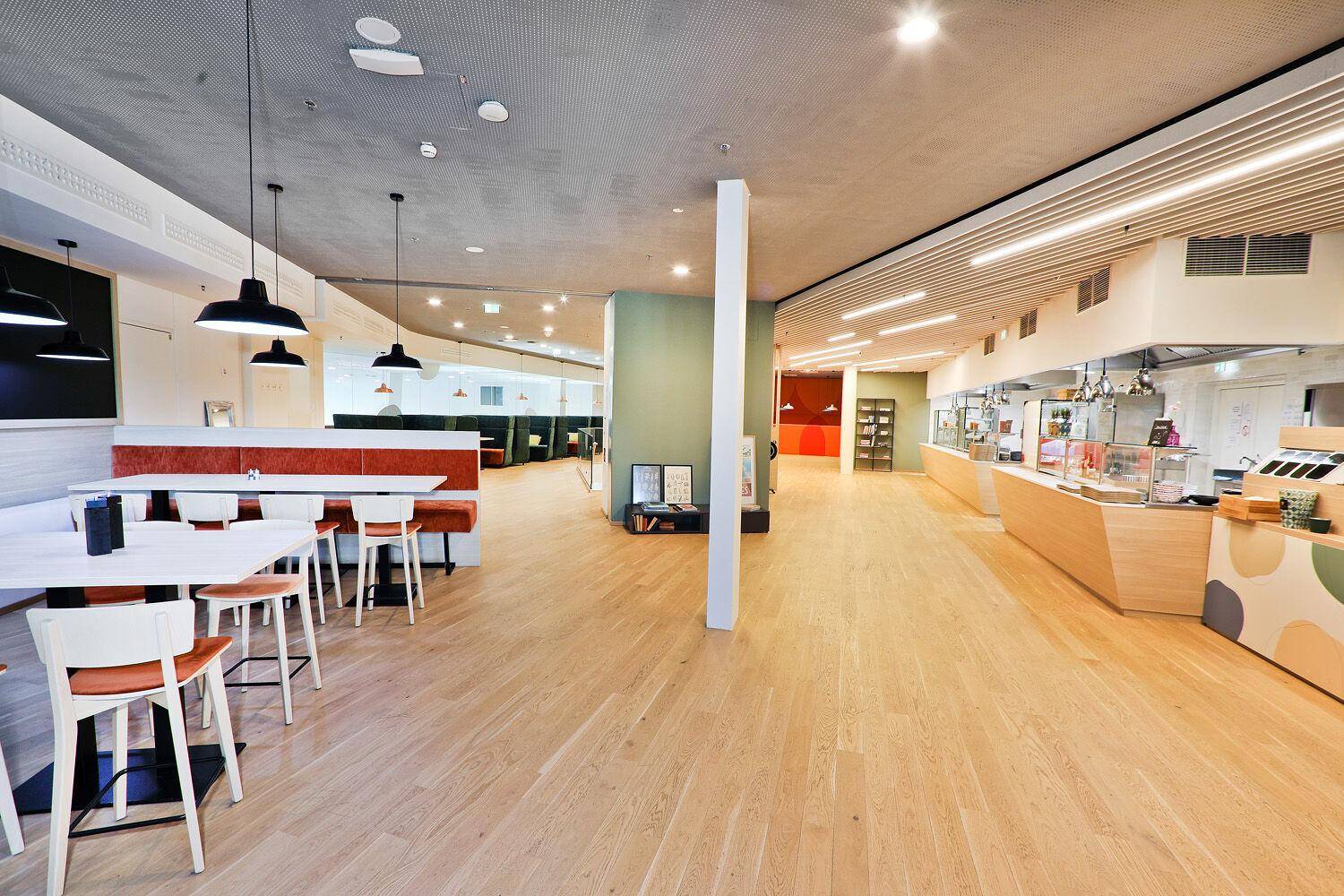 Geräumige Kantine mit langen Tischen, Sitzbänken und einer modernen Essensausgabe.