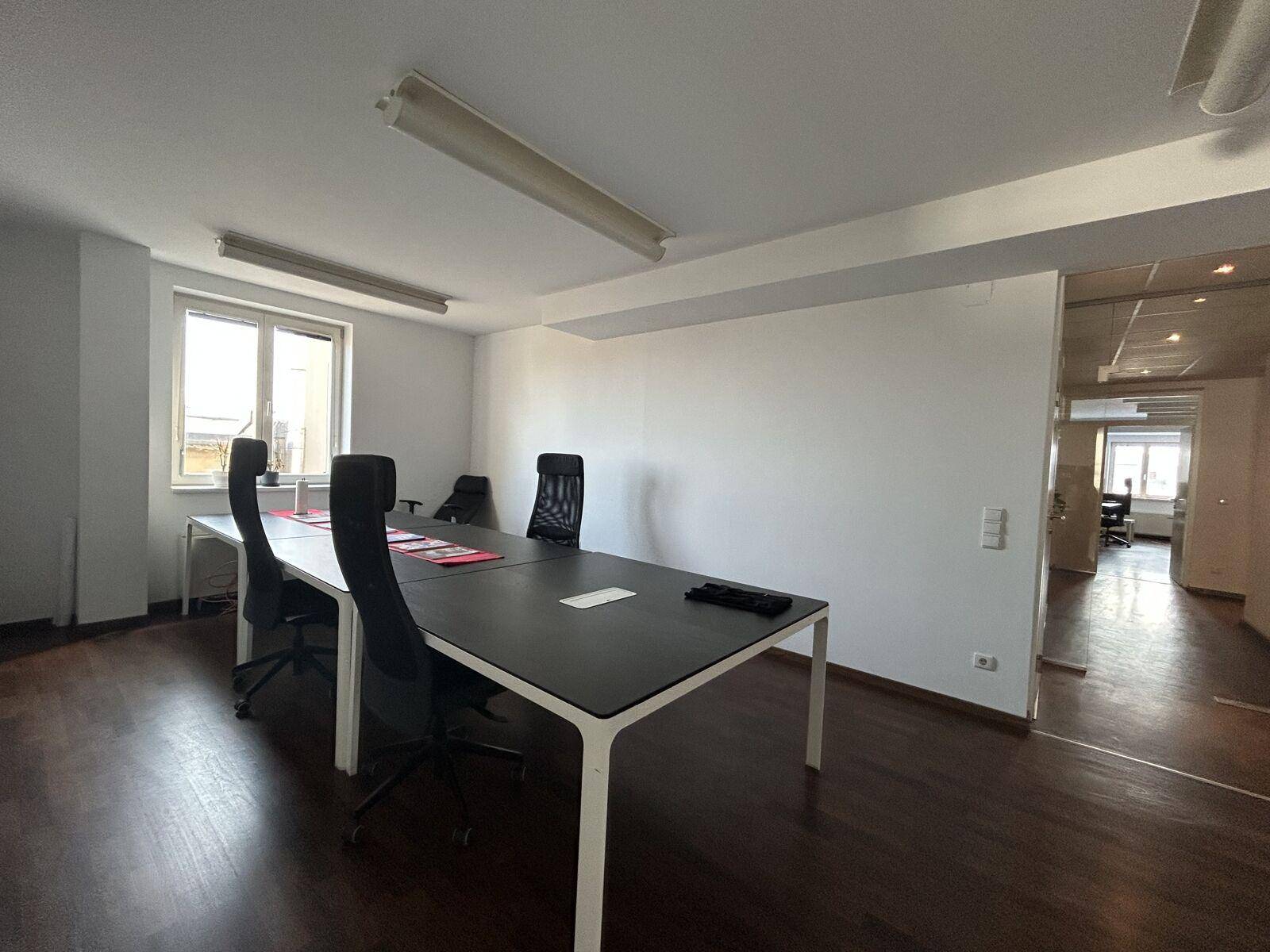 Modernes Büro mit dunklem Laminatboden, weißen Wänden und zwei Arbeitsplätzen mit ergonomischen Stühlen.