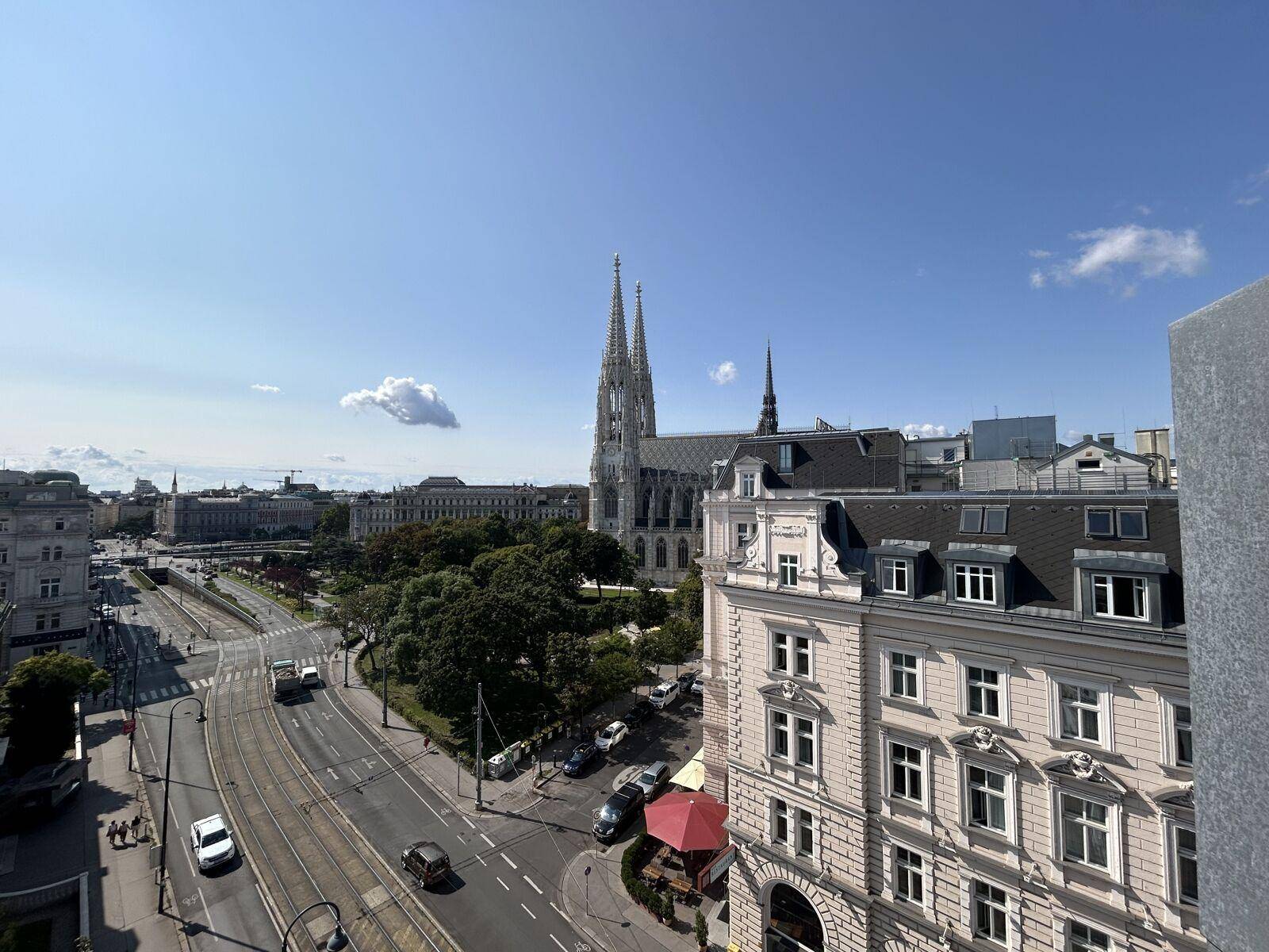 Panoramablick über die Stadt mit historischen Gebäuden, einer Kirche und einer belebten Straße unter blauem Himmel.