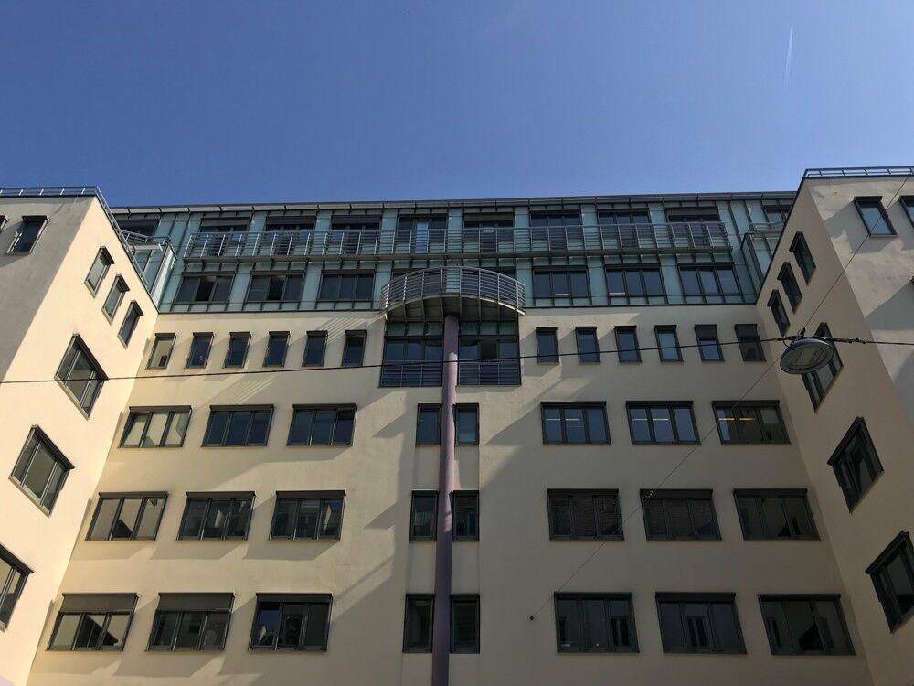 Moderne Gebäudefassade mit vielen Fenstern und einem kleinen Balkon unter klarem blauem Himmel.