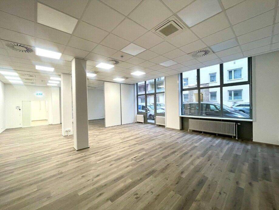 Geräumiger Gewerberaum mit großen Fenstern, modularen Trennwänden und modernem Bodenbelag.