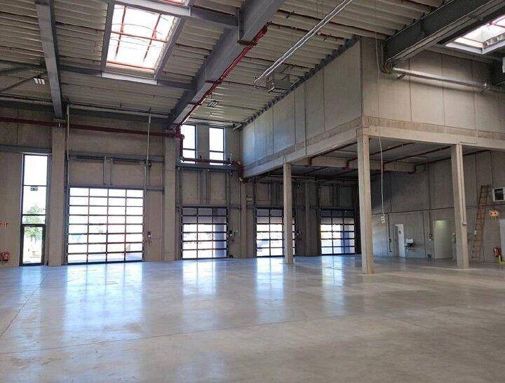 Große Lagerhalle mit mehreren Rolltoren, hohen Decken und einem Zwischengeschoss, bereit zur Nutzung.