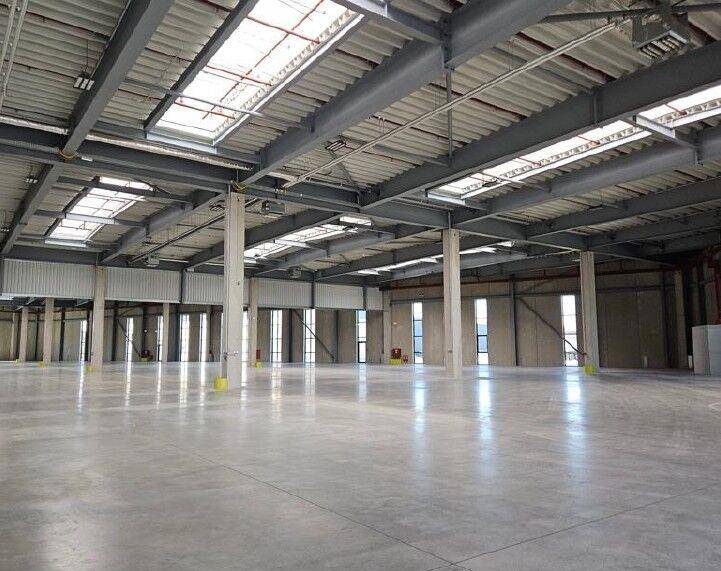 Weitläufige Lagerhalle mit Betonboden, Stahlskelett und Oberlichtern, die viel Tageslicht hereinlassen.