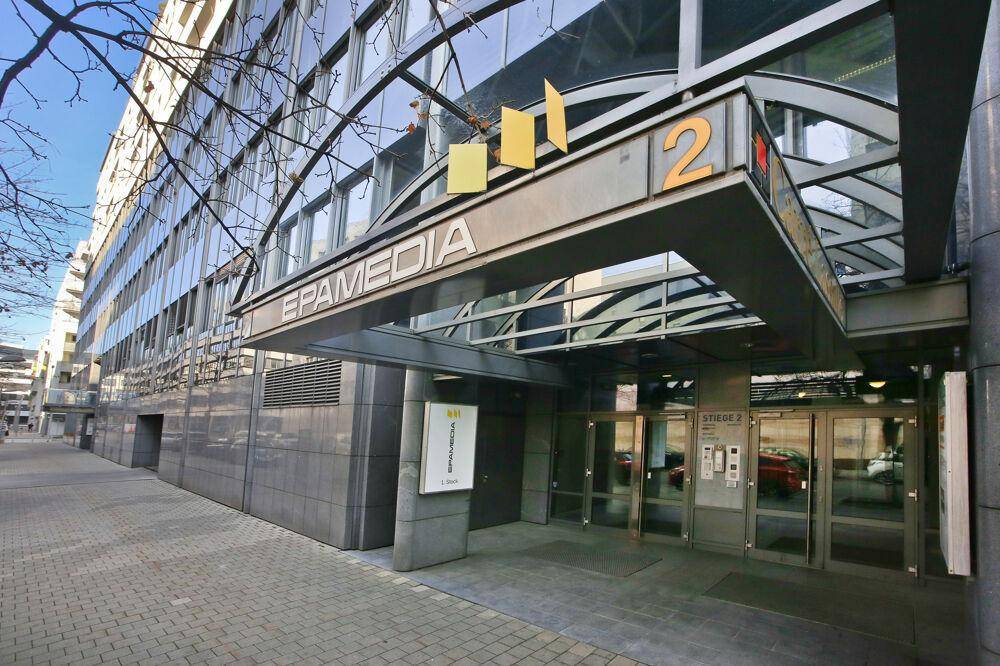 Moderner Gebäudeeingang mit geschwungener Glasüberdachung und Firmenlogo an der Fassade.