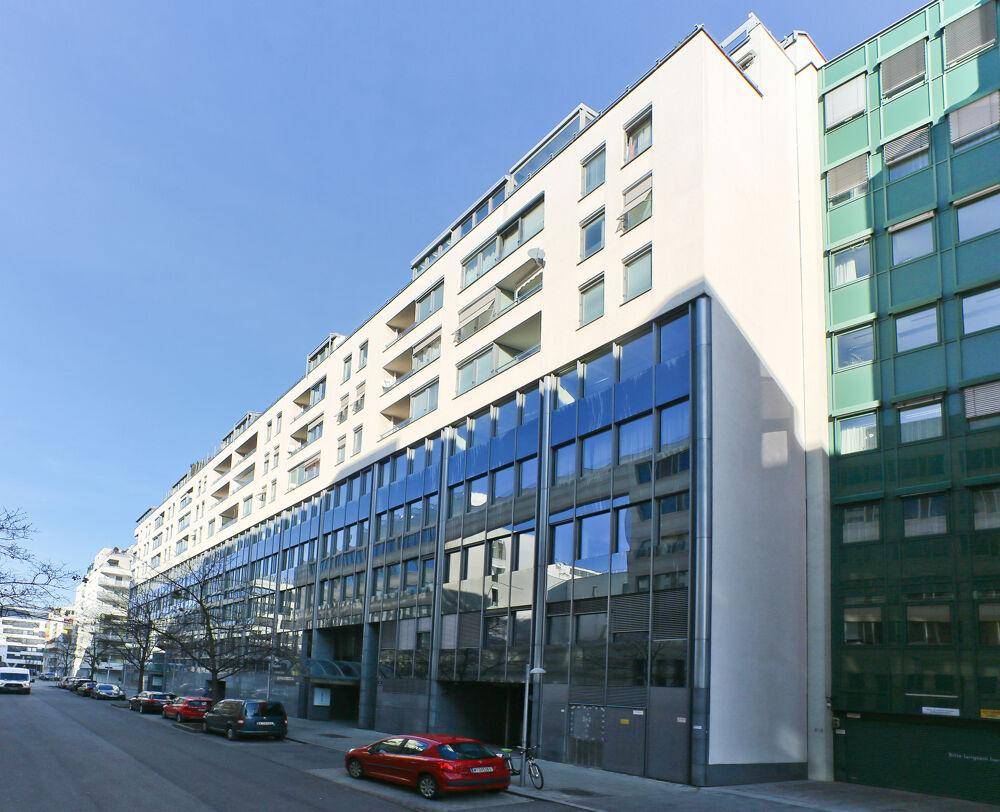 Langes, modernes Gebäude mit durchgehender Glasfront im unteren Bereich und Balkonen in den oberen Etagen.