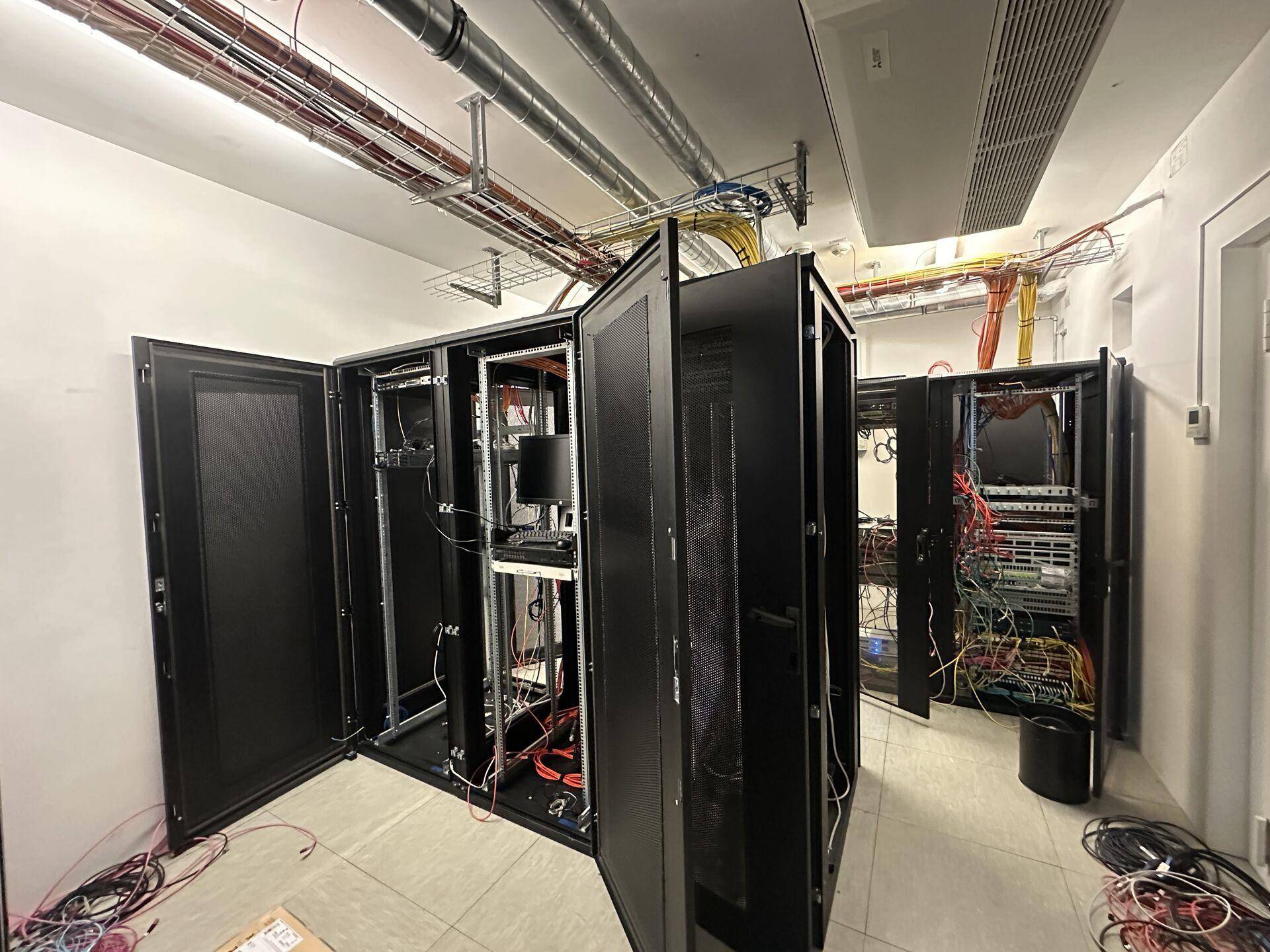 Serverraum mit offenen Racks, sichtbaren Kabeln und technischen Installationen an der Decke.