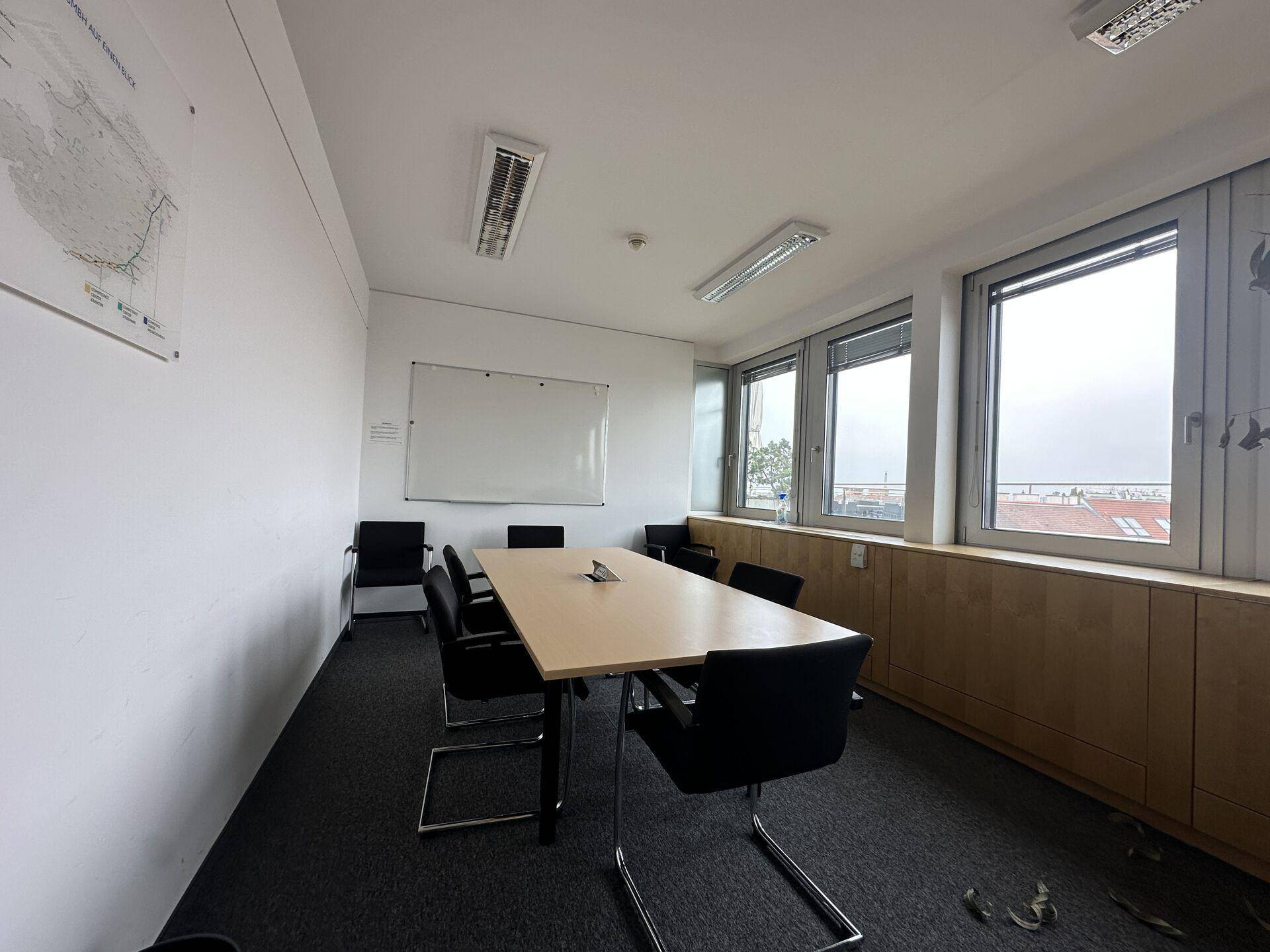 Konferenzraum mit Holztisch, schwarzen Stühlen, Whiteboard und Fenstern mit Blick auf die Stadt.