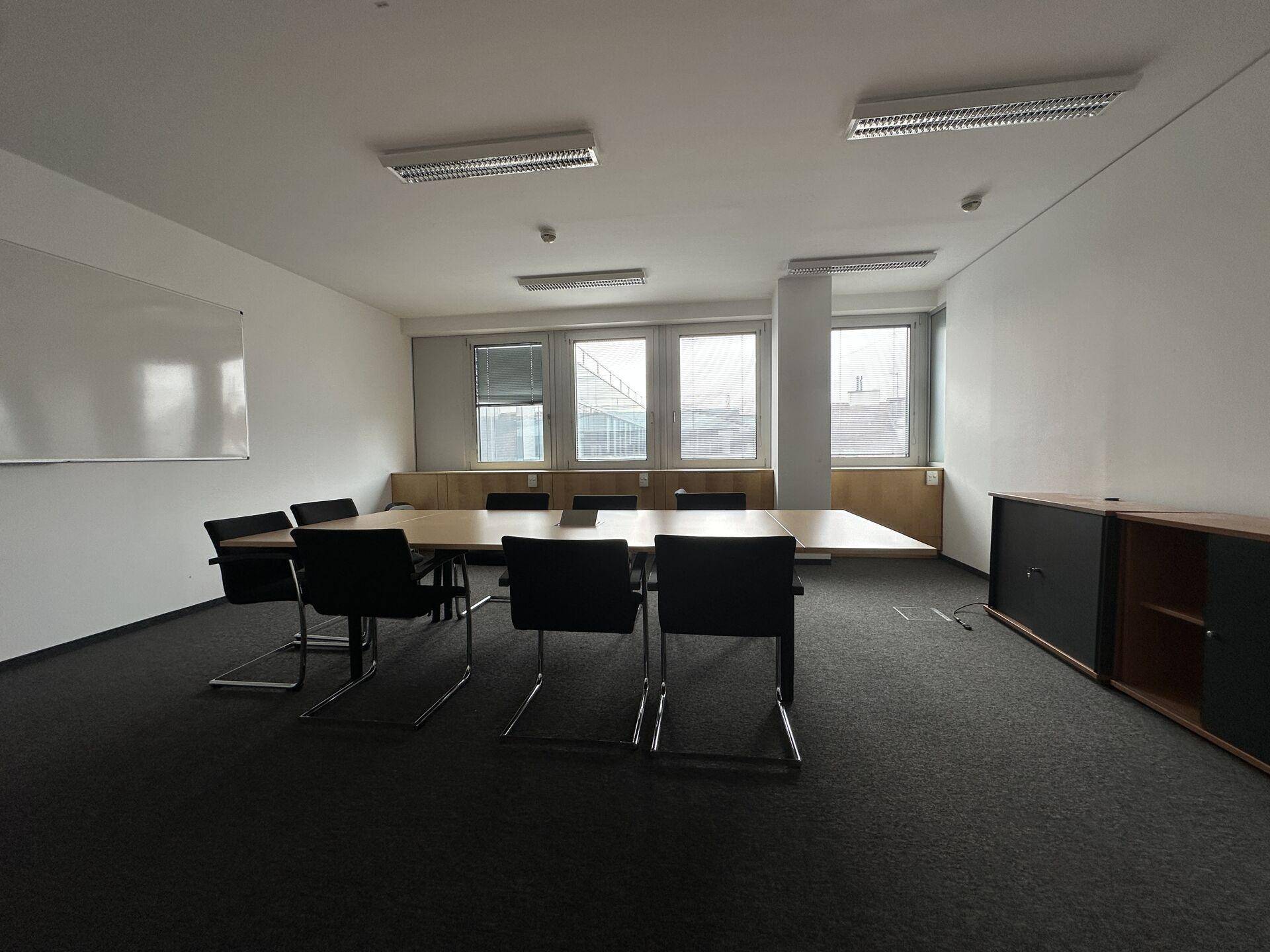 Konferenzraum mit langem Holztisch, schwarzen Stühlen und Schränken an der Wand.