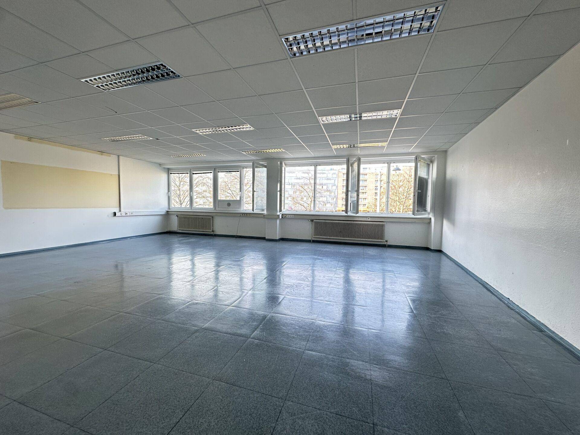 Geräumiges, leeres Büro mit großen Fenstern, die einen Blick auf die Umgebung und Bäume ermöglichen.