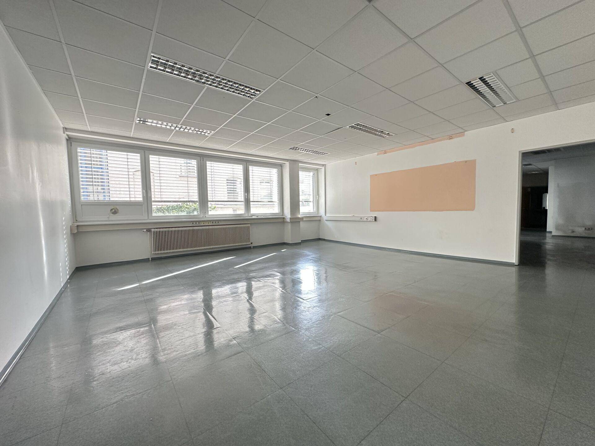 Geräumiges, leeres Büro mit großen Fenstern und einer hellen Wandtafel, ideal für Besprechungen.