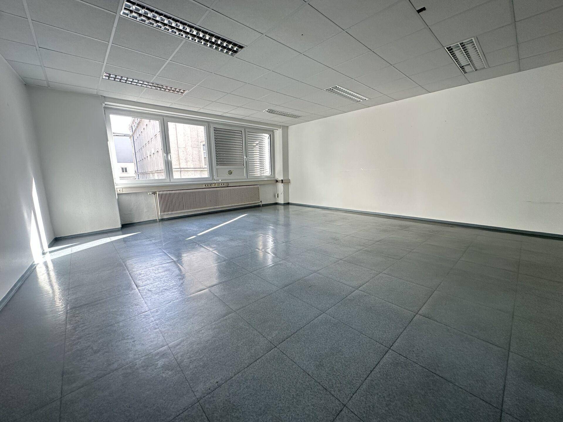Leeres Büro mit großen Fenstern, die viel Sonnenlicht hereinlassen und einen Blick auf die Stadt bieten.