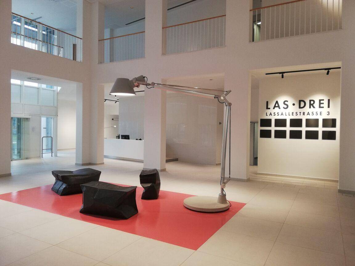 Geräumige, moderne Lobby mit hohen Decken, minimalistischer Einrichtung und einer auffälligen Stehlampe.