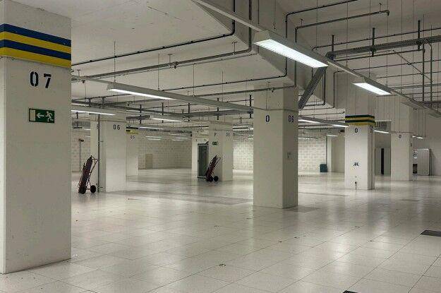 Große, leere Tiefgarage mit Fliesenboden, vielen Säulen und sichtbaren Installationen an der Decke.