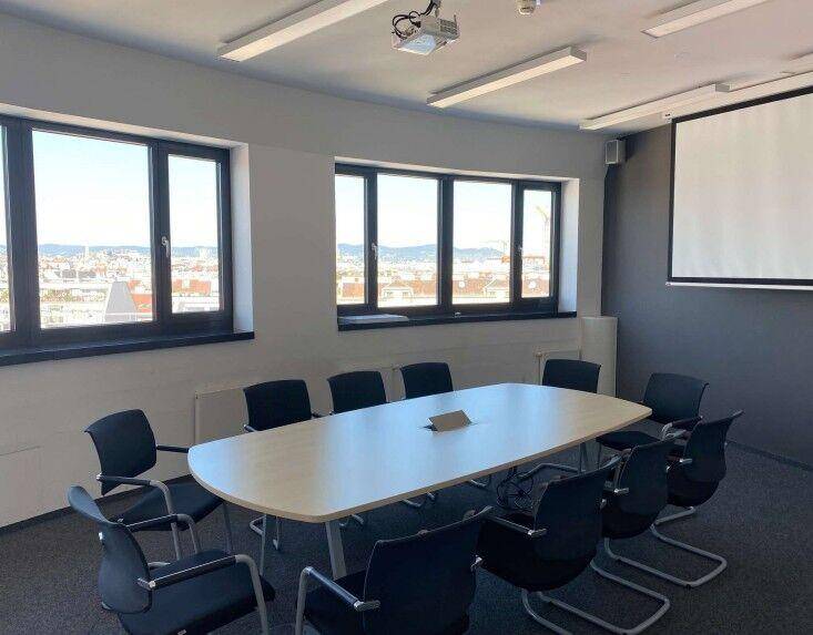 Moderner Konferenzraum mit großem Tisch, Projektor und weitem Blick über die Stadt durch große Fenster.