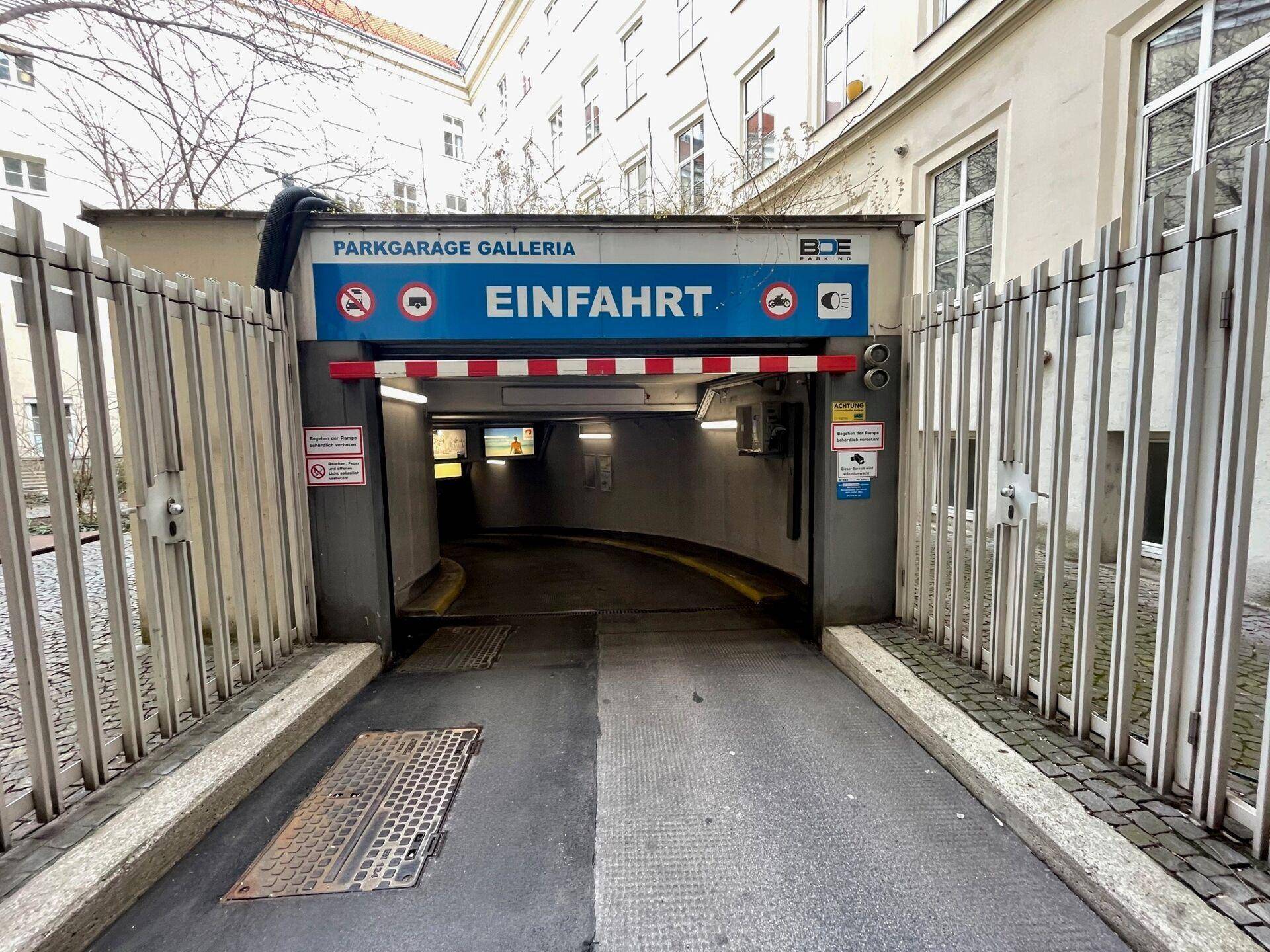Einfahrt zu einer Tiefgarage mit Beschilderung und Metallgittern, die den Zugang sichern.