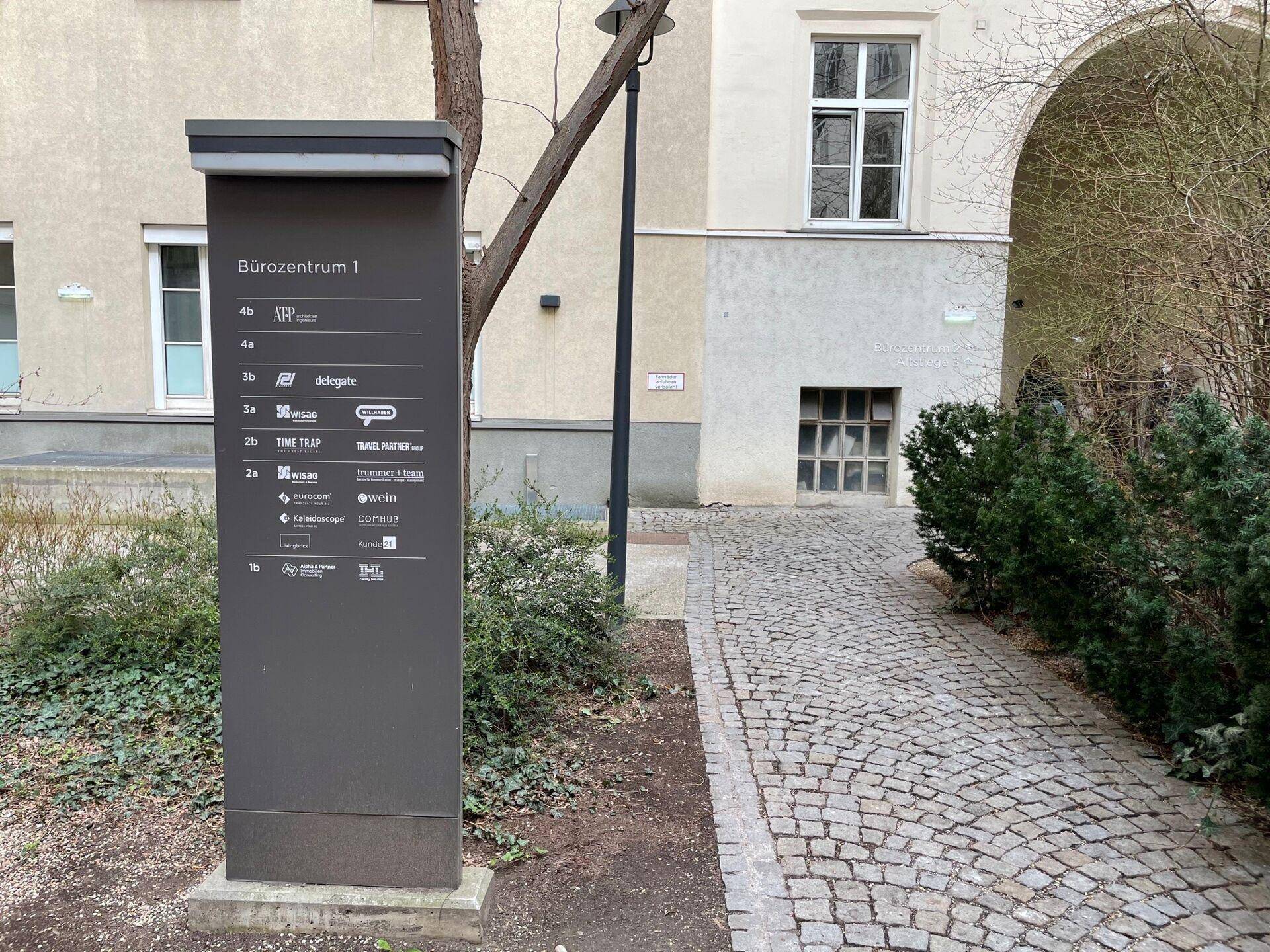 Außenbereich mit einem Weg aus Kopfsteinpflaster und einem Schild, das ein Bürozentrum anzeigt.