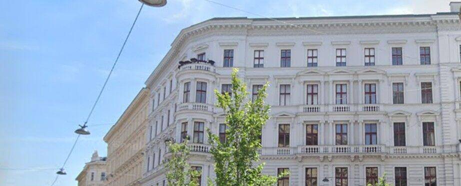 Historisches Gebäude mit klassischer Architektur, vielen Fenstern und einem kleinen Balkon im oberen Bereich.