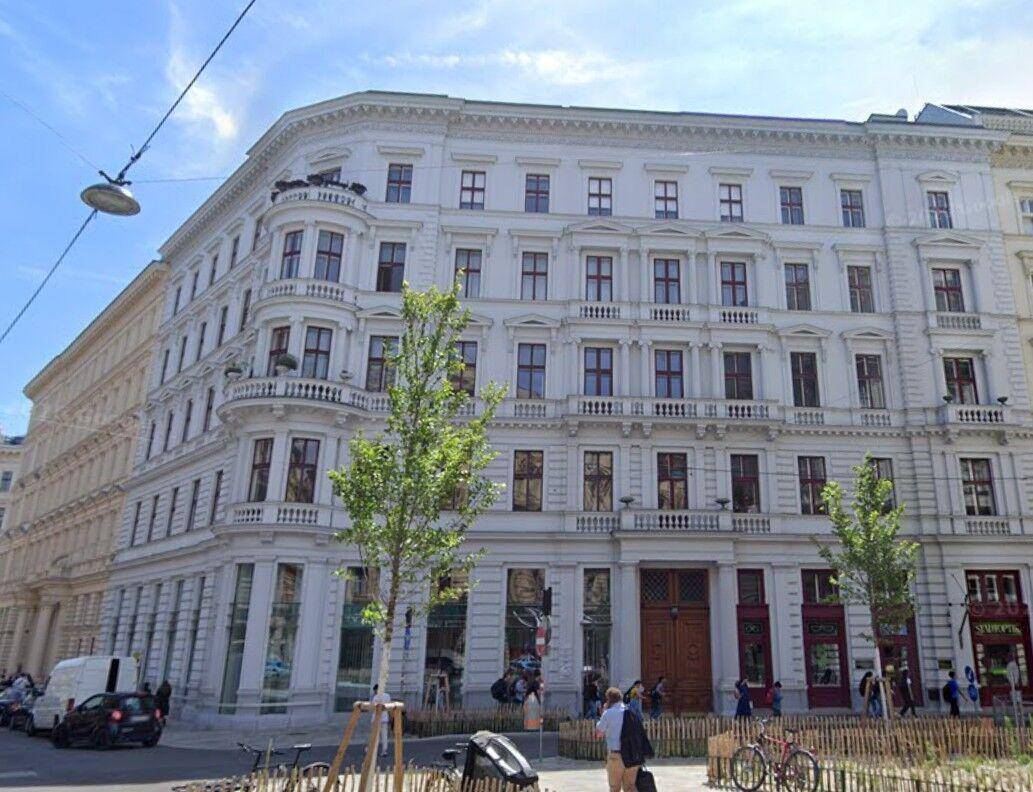 Elegantes Eckgebäude mit historischer Fassade, großen Fenstern und Geschäften im Erdgeschoss an einer belebten Straße.