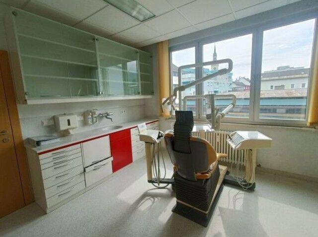 Behandlungszimmer mit zahnmedizinischer Ausstattung, großen Fenstern und Blick auf die Stadt.