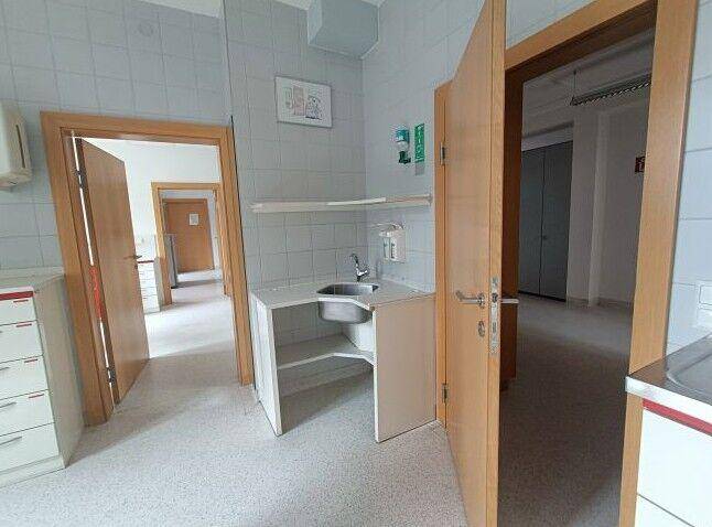 Kleiner Behandlungsraum mit Waschbecken, Fliesenwänden und zwei offenen Holztüren.