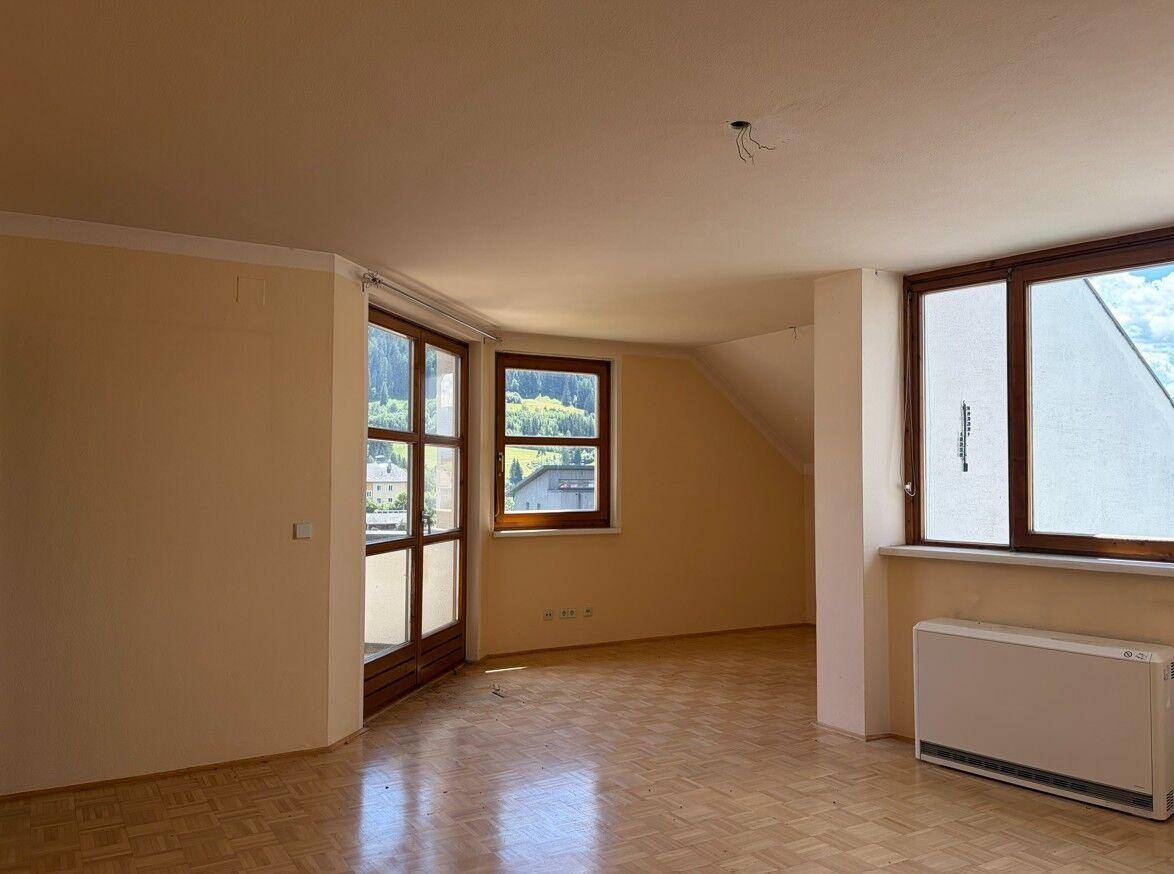 Heller Wohnraum mit Parkettboden, großen Fenstern und Zugang zu einem Balkon oder einer Terrasse.
