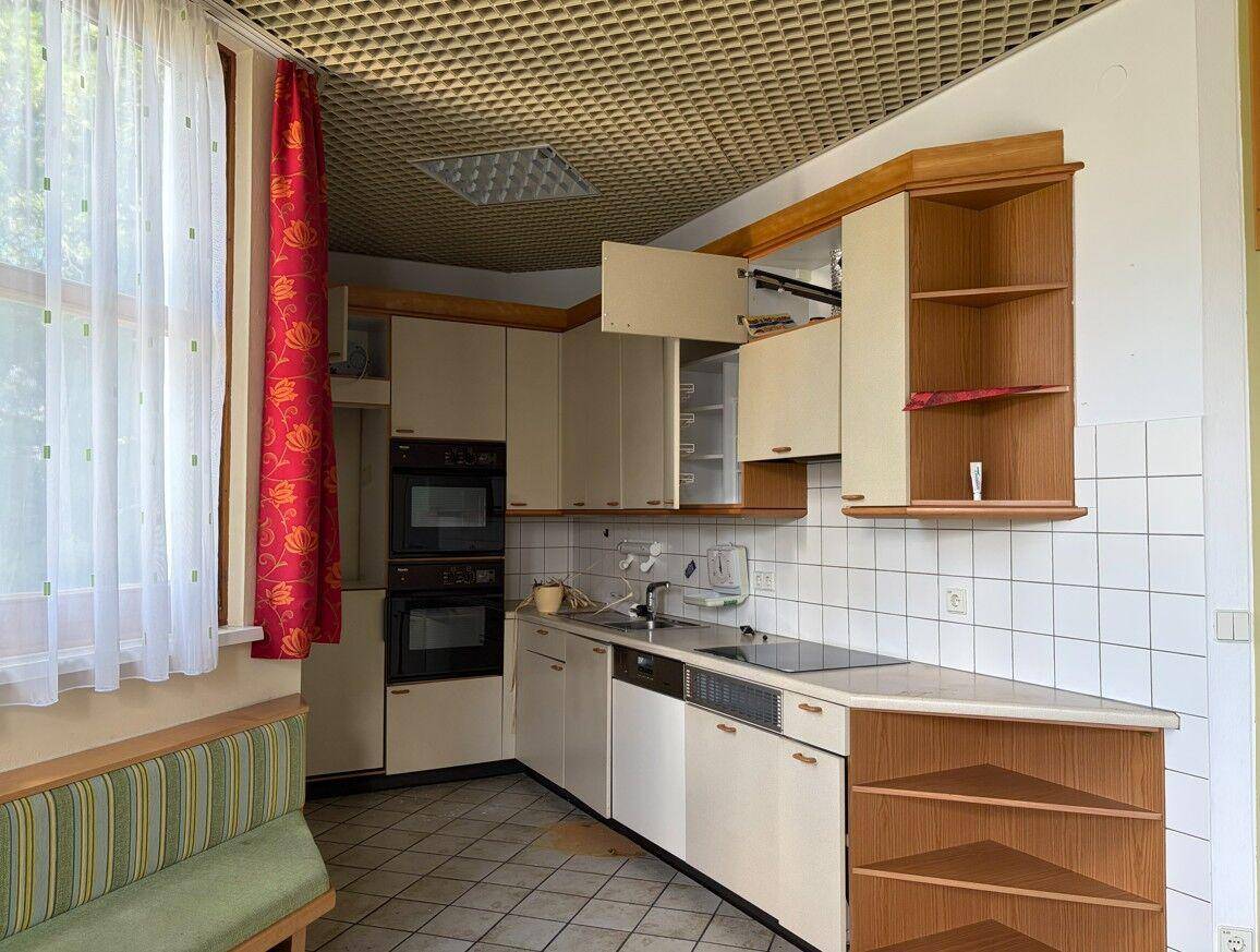 Ältere Einbauküche mit zwei Öfen, Kochfeld und Spüle, ausgestattet mit weißen Fliesen und Holzschränken.