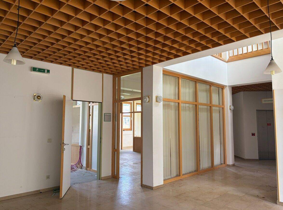 Geräumiger Flur mit Holzgitterdecke, großen Fenstern und Zugang zu mehreren Büroräumen.