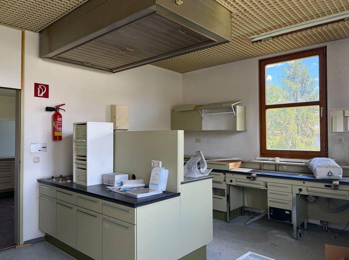 Funktionale Küche mit Arbeitsplatten, Spüle und einem großen Fenster, das viel Tageslicht hereinlässt.