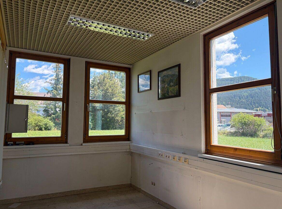 Helles Büro mit drei großen Fenstern, die einen Blick ins Grüne bieten, und einer Gitterdecke.