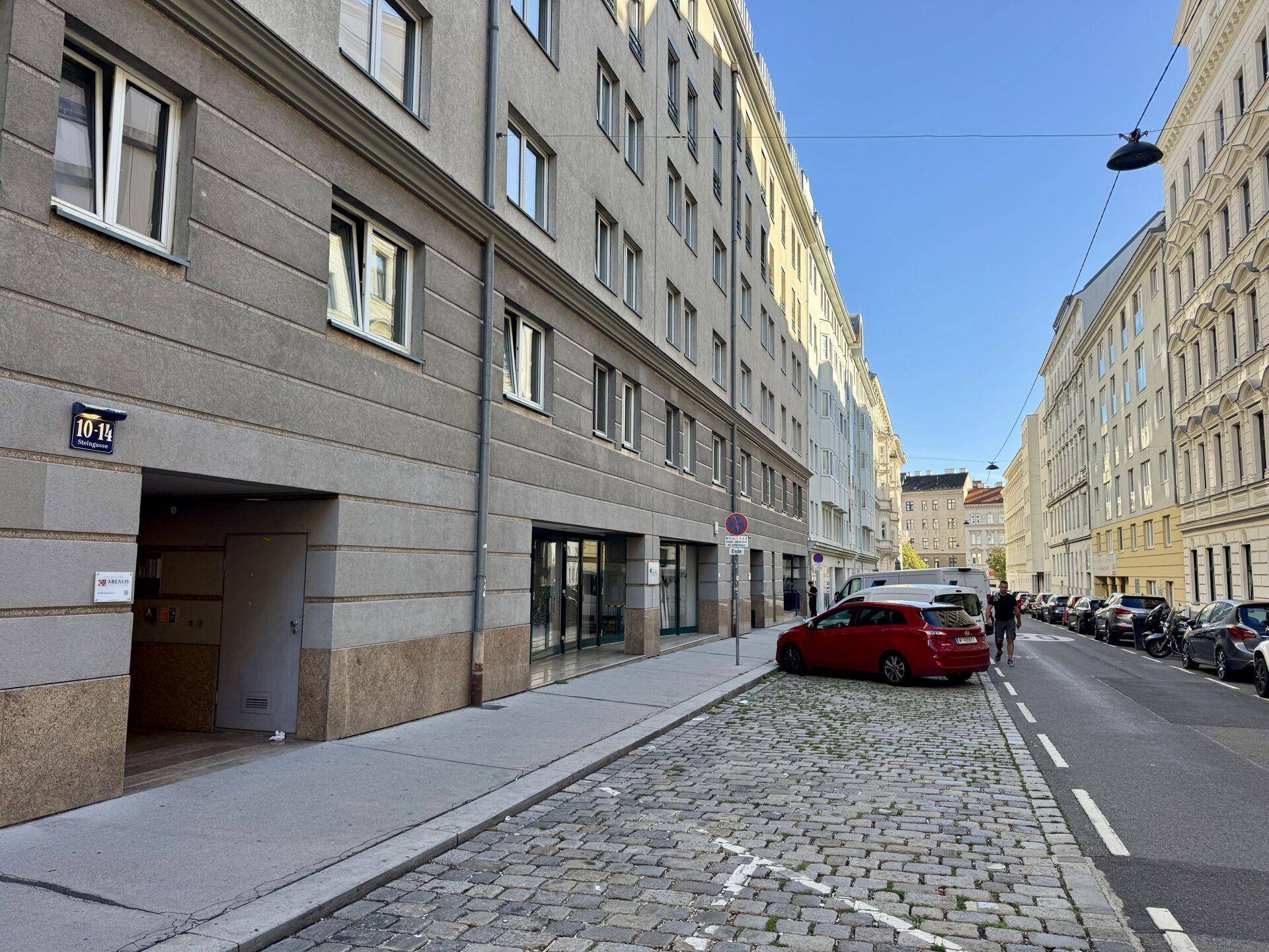 Blick auf eine belebte Straße mit geparkten Autos und der Fassade eines Mehrfamilienhauses.
